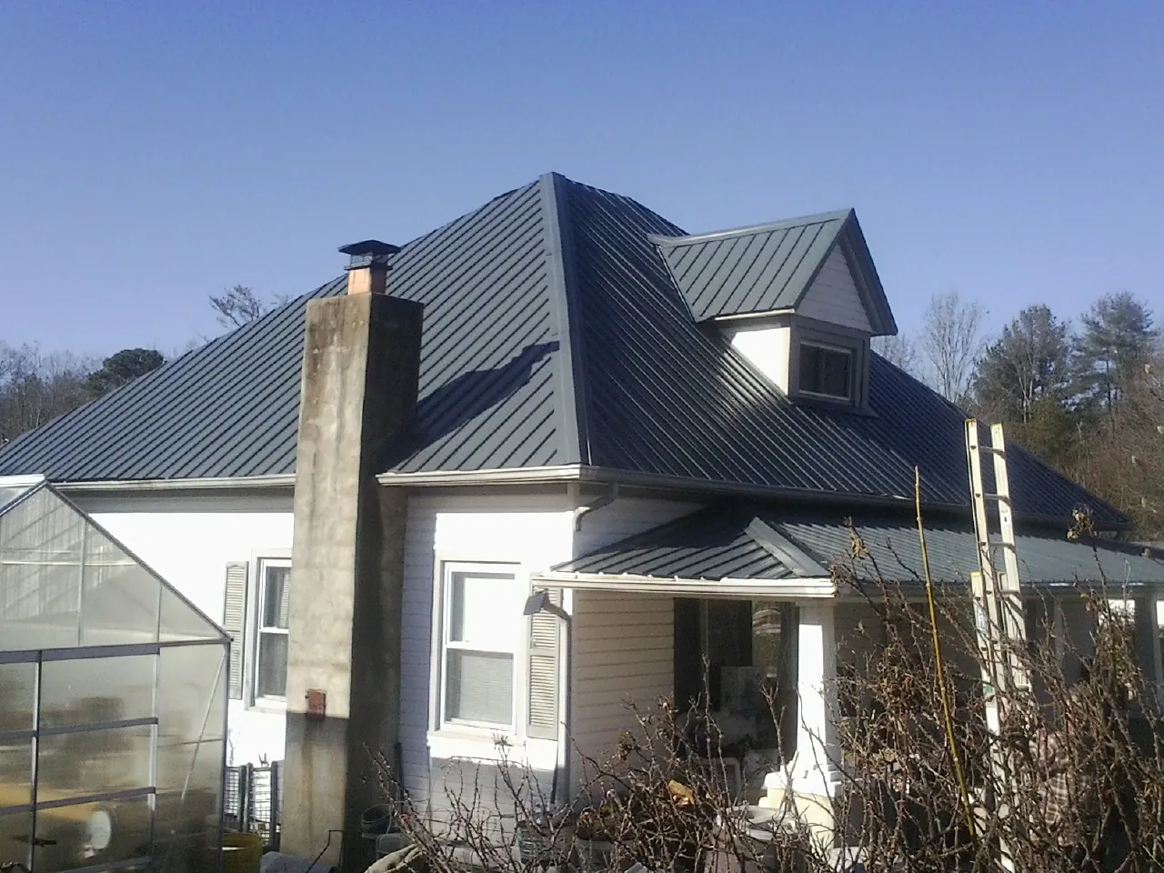 Dark blue standing seam metal roof on a white farmhouse with dormer in Windsor