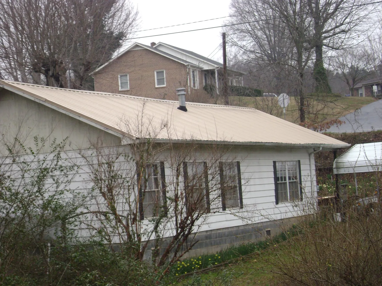 Tan metal roof on a white sided house set into a hillside — Commercial Roofing by Roofing Brothers in Windsor